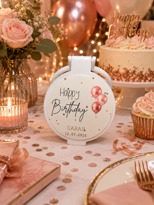 Personalised white compact mirror favour featuring a Happy Birthday design with pink balloons, personalised name and date, displayed on an elegant pink and rose-gold birthday table.