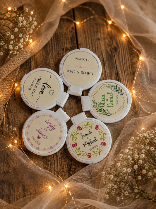 Personalised wedding compact mirror favours in five designs arranged on rustic wood with wedding fabric and warm fairy lights